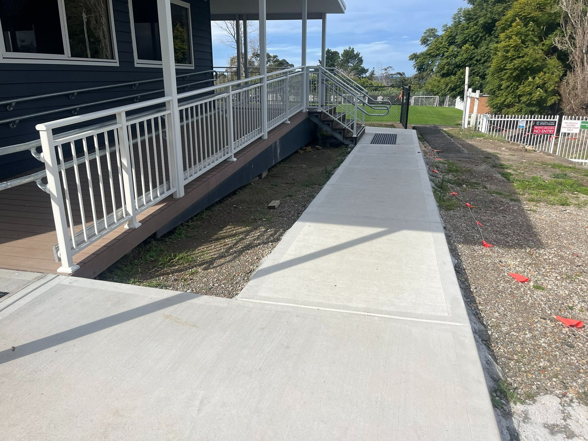 A concrete walkway next to a building with a white railing and gravel border.