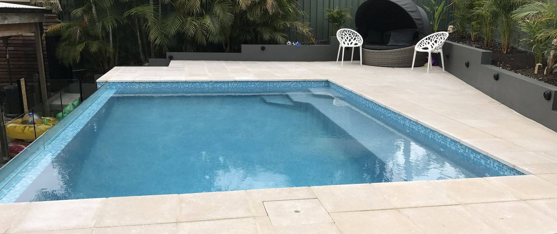 A backyard with a pool, patio, and lounge area. The pool has blue mosaic tiles.