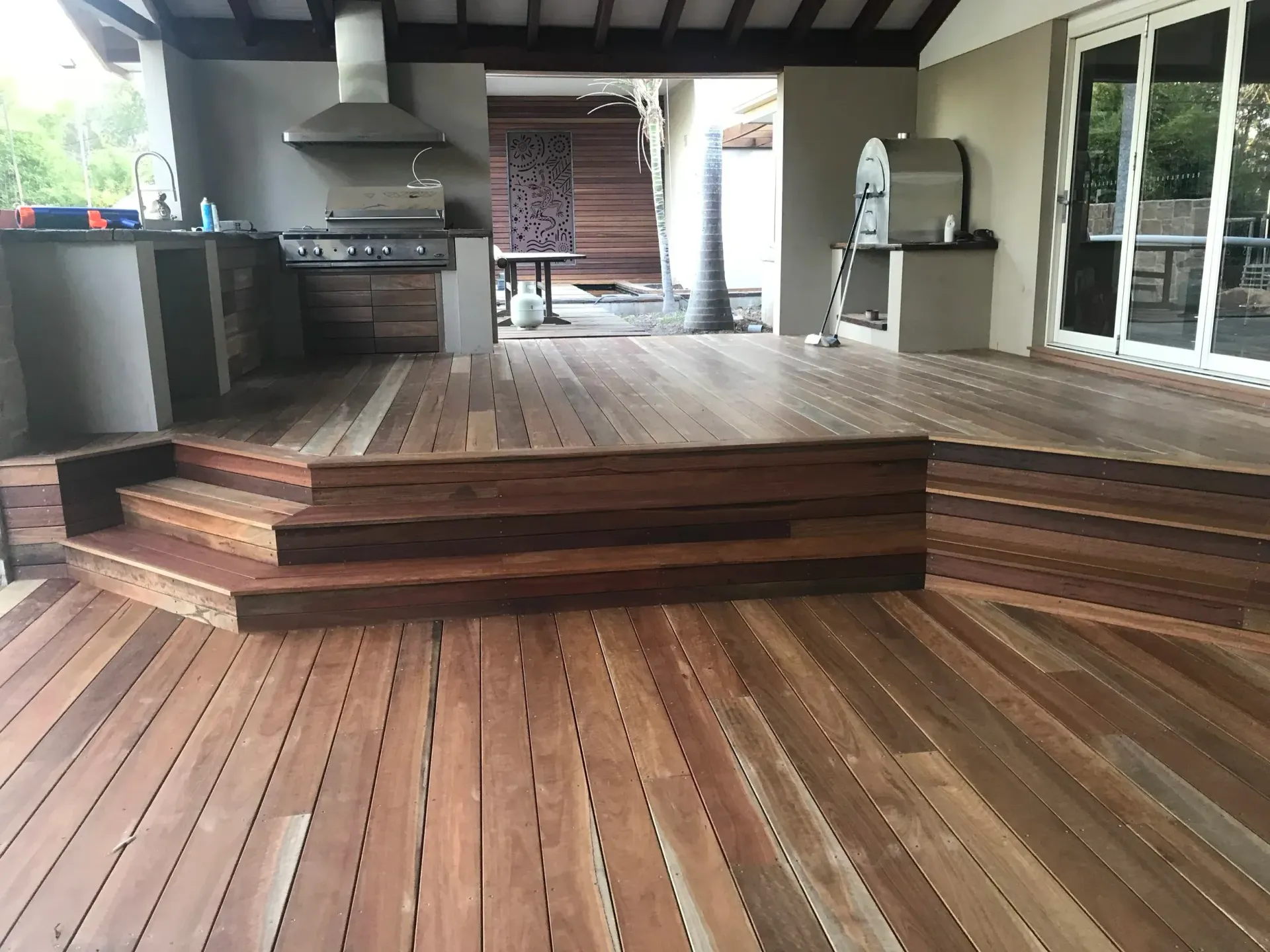 Outdoor wooden deck with steps leading to a kitchen area with a grill and stainless steel appliances.
