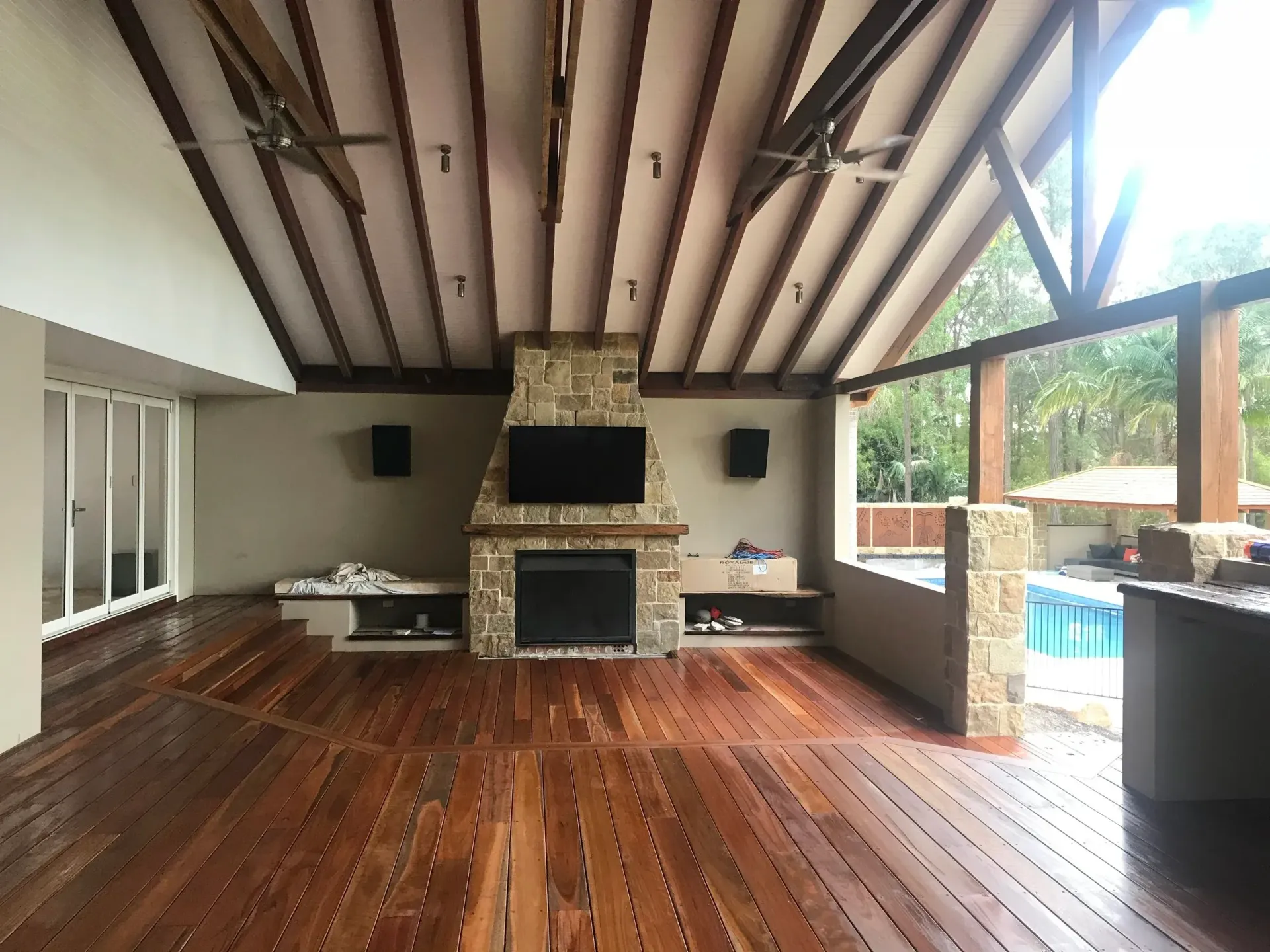 Patio with wooden floor, stone fireplace, TV, speakers, and view of a pool.