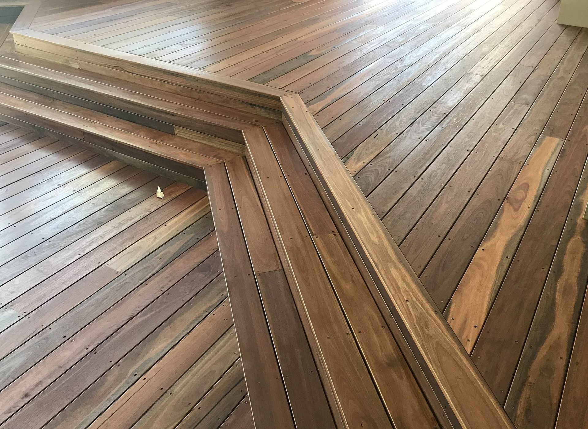 Wooden deck with built-in stairs and handrail. Angled planks create a geometric pattern.