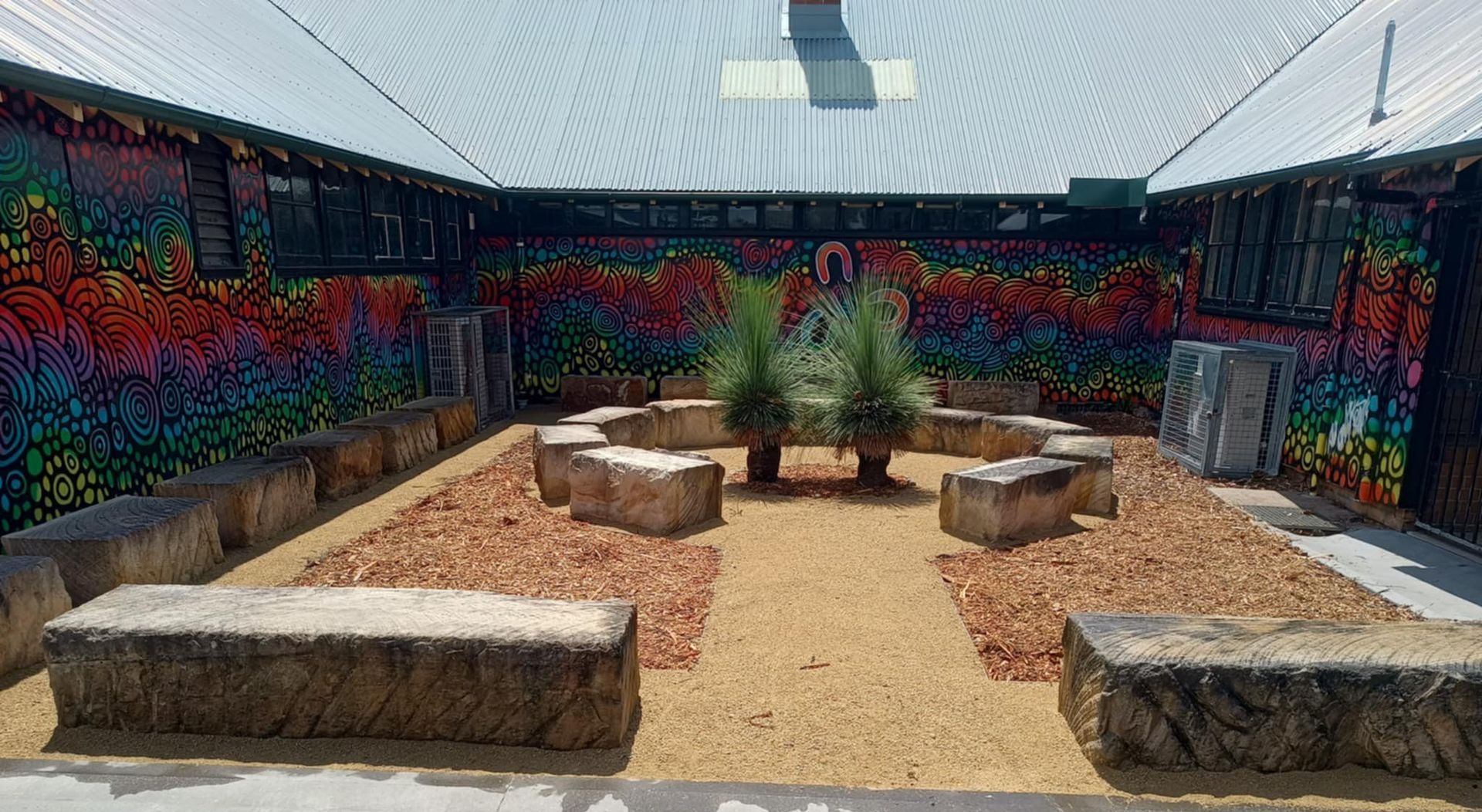 Courtyard with colorful mural, stone benches, and a central garden bed with plants.