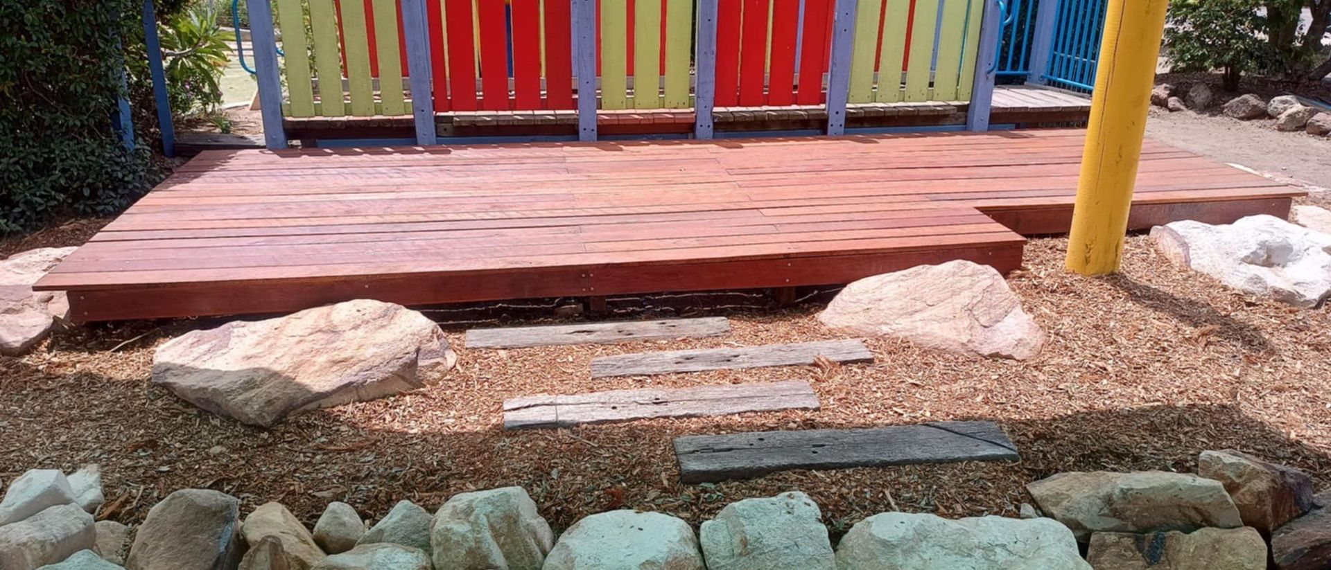 Wooden deck with painted fence, rock steps, and gravel ground.