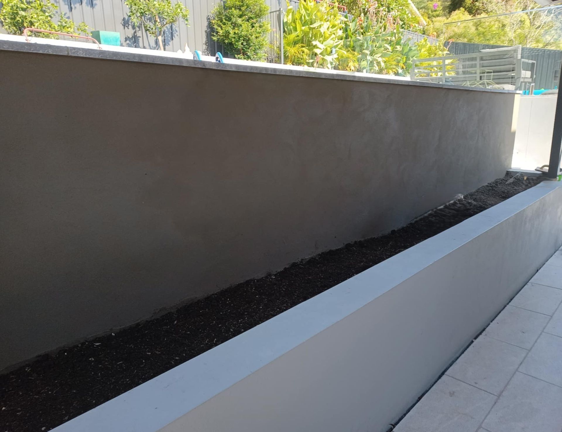 Gray stucco wall with a white planter box filled with dark soil; outdoor setting.