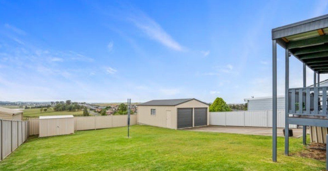 Grassy backyard with a garage, wooden fence, and partly cloudy blue sky.