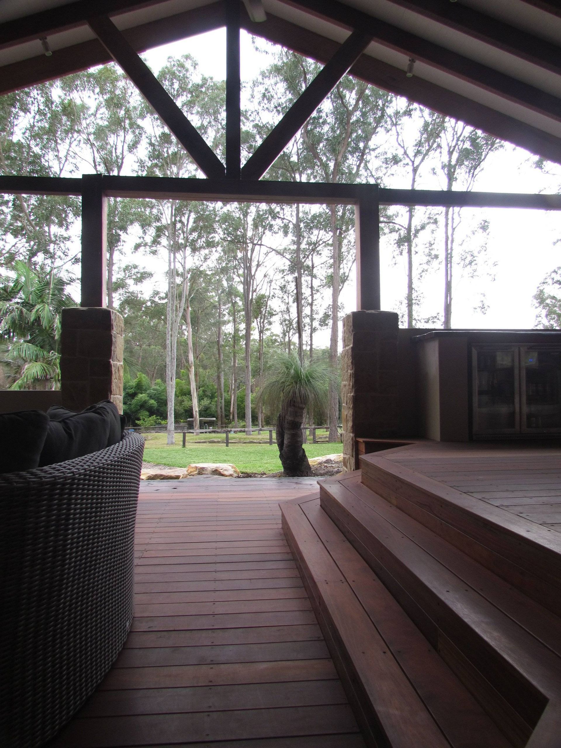 Covered patio with wooden deck, overlooking a green yard and tall trees.