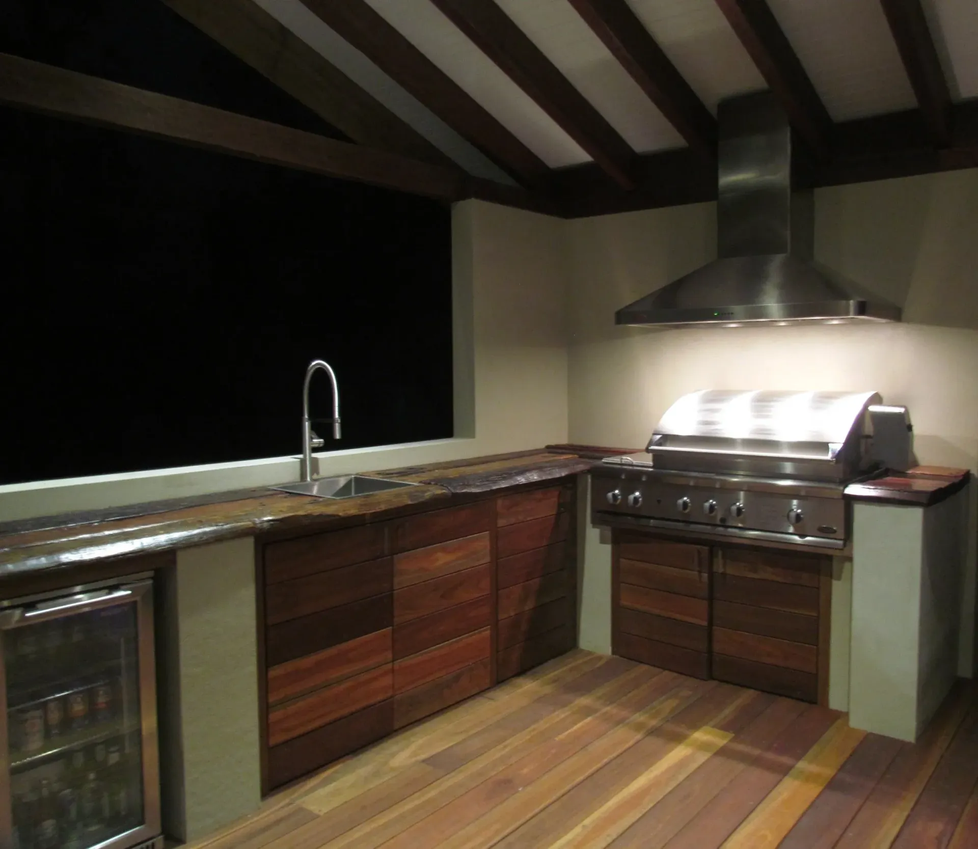 Outdoor kitchen with built-in grill, sink, and cabinetry under a wooden pergola.