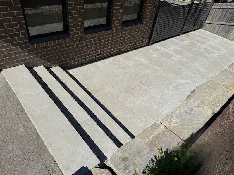 Concrete patio with steps, brick wall, and dark fence.