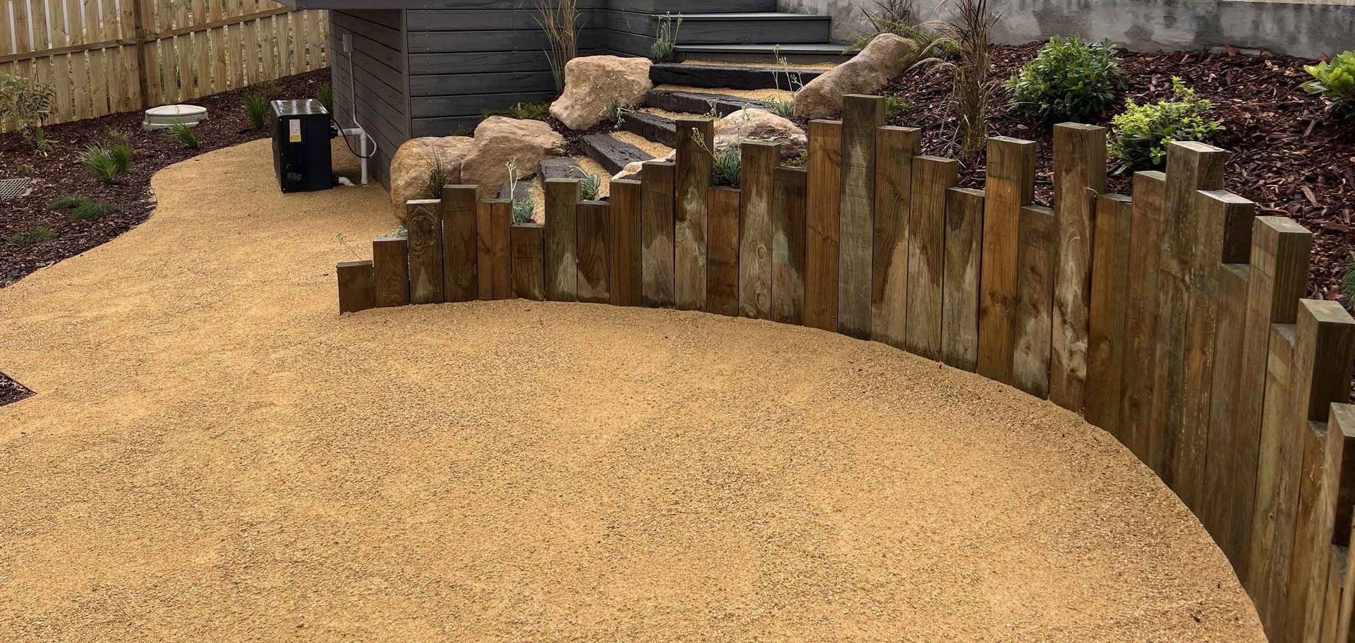 Curved wooden fence surrounding a gravel yard. A path leads from the fence to the left side.