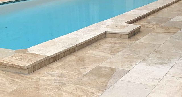 Poolside view: Light-colored stone patio bordering a turquoise pool. Small raised stone platform.