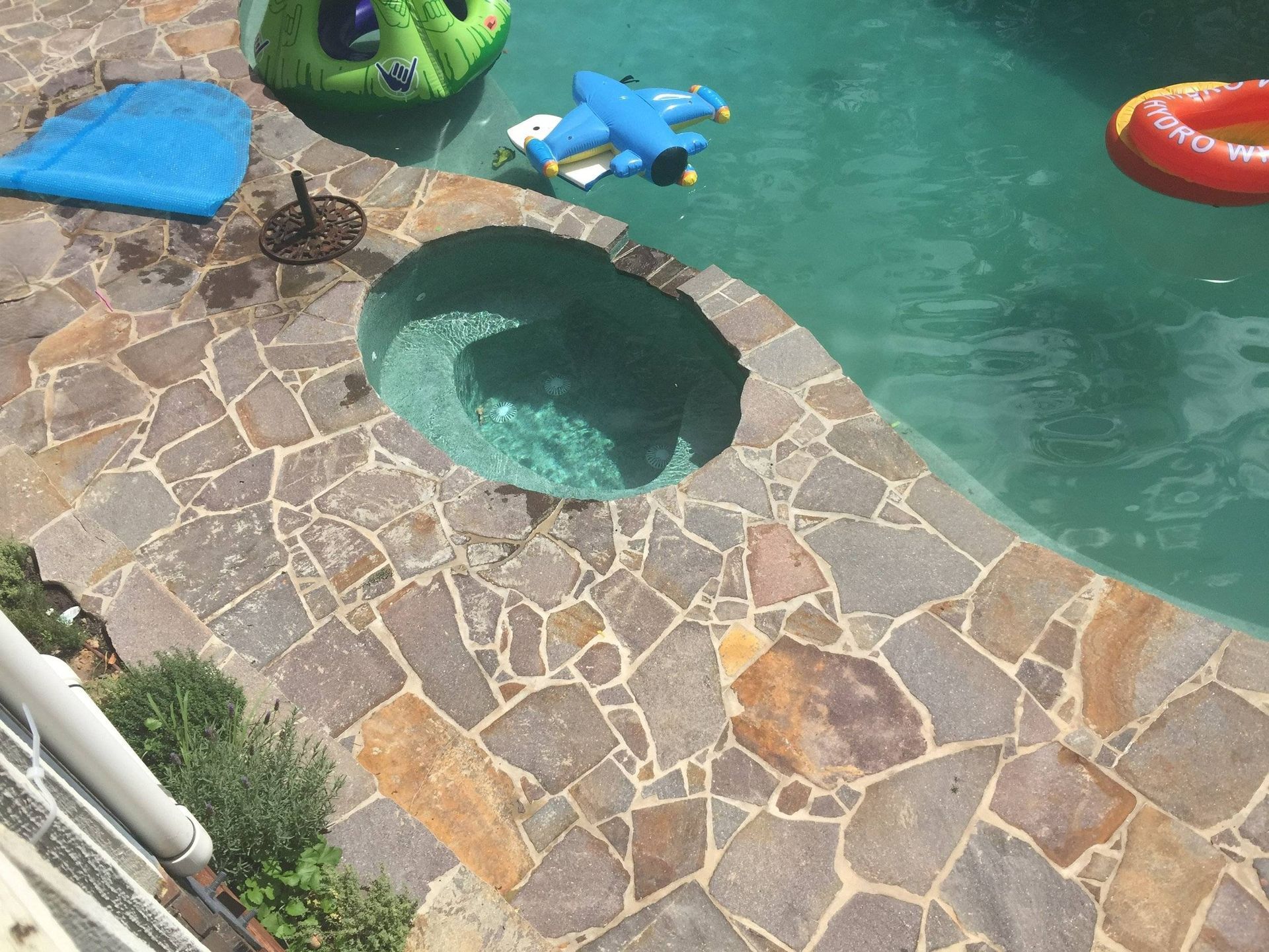 Pool with stone coping, a small attached hot tub, and floating inflatables in the water.