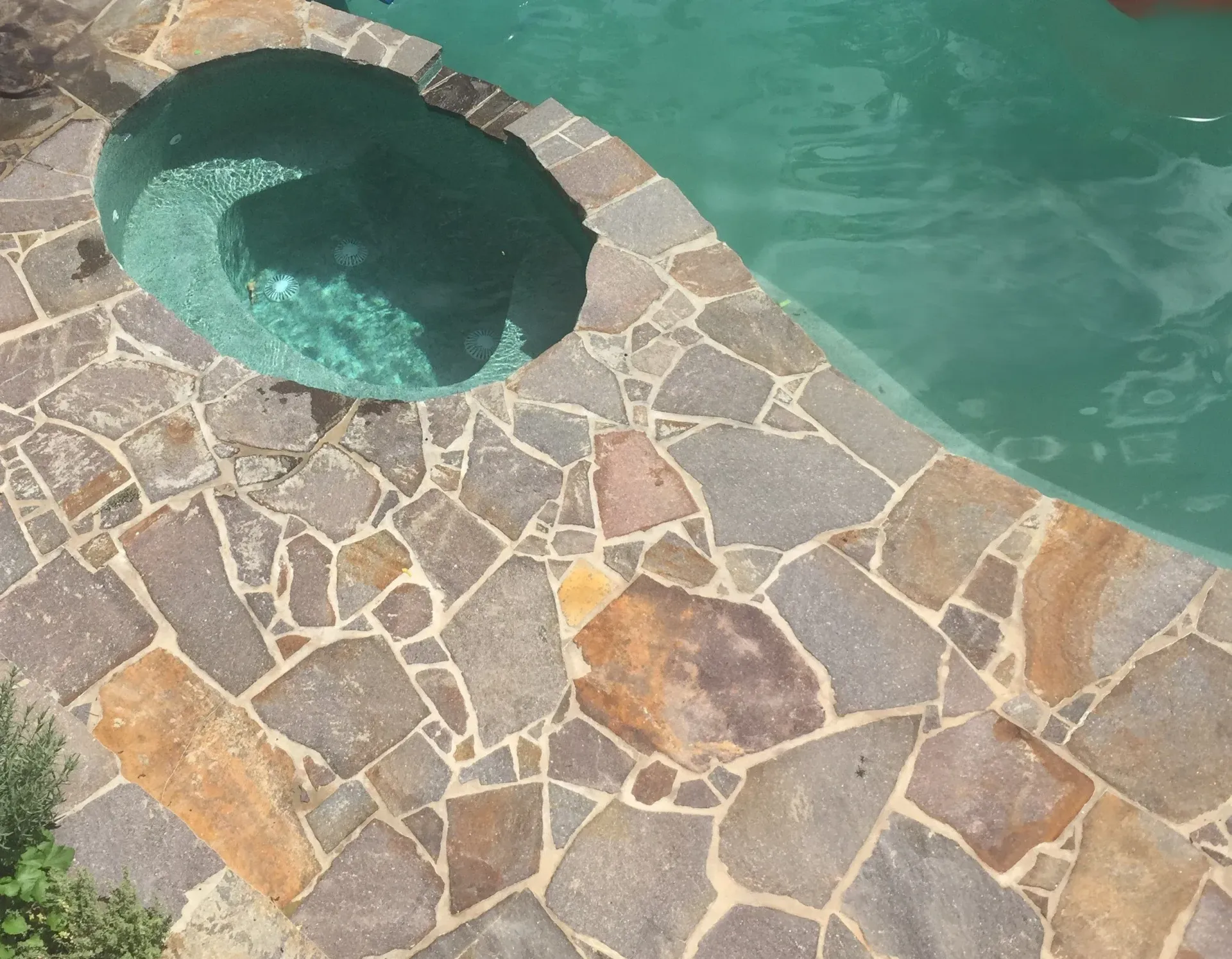 Stone patio with pool and spa, turquoise water, earth-tone tiles.