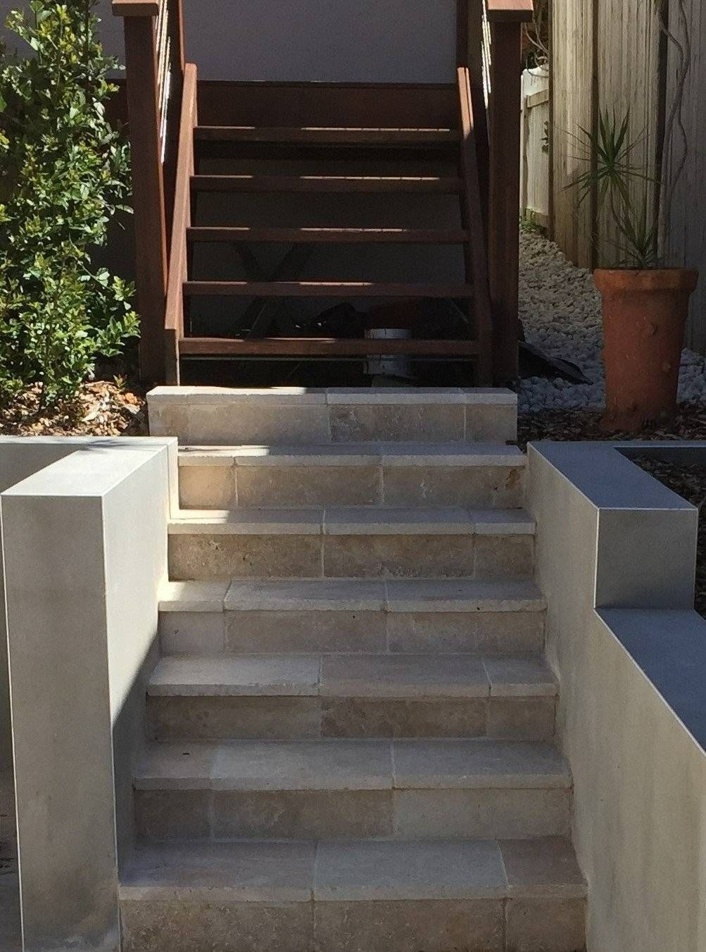 Stone steps leading up to wooden stairs with a brown handrail, outdoor setting.