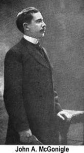 John A. McGonigle, in a dark suit, stands in profile, hand on a desk.