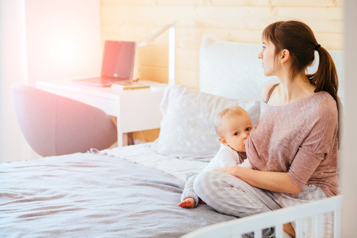 A woman is sitting on a bed holding a baby.
