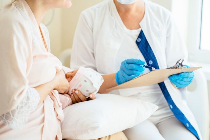 A woman is holding a baby and talking to a doctor who is holding a clipboard.