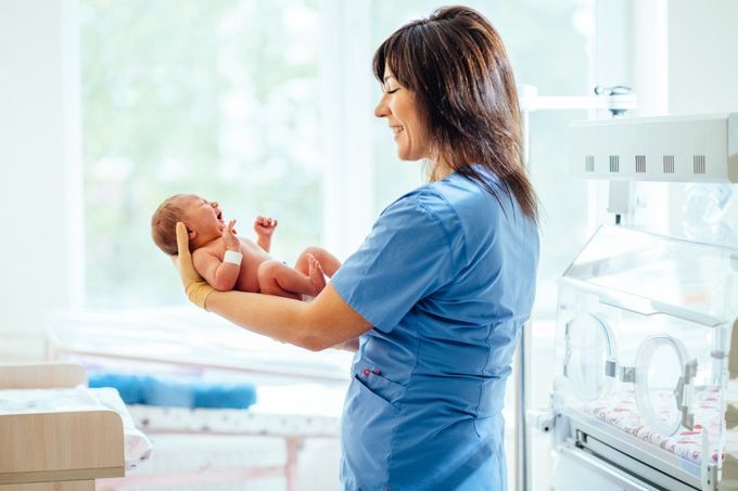 A nurse is holding a newborn baby in her arms in a hospital room.