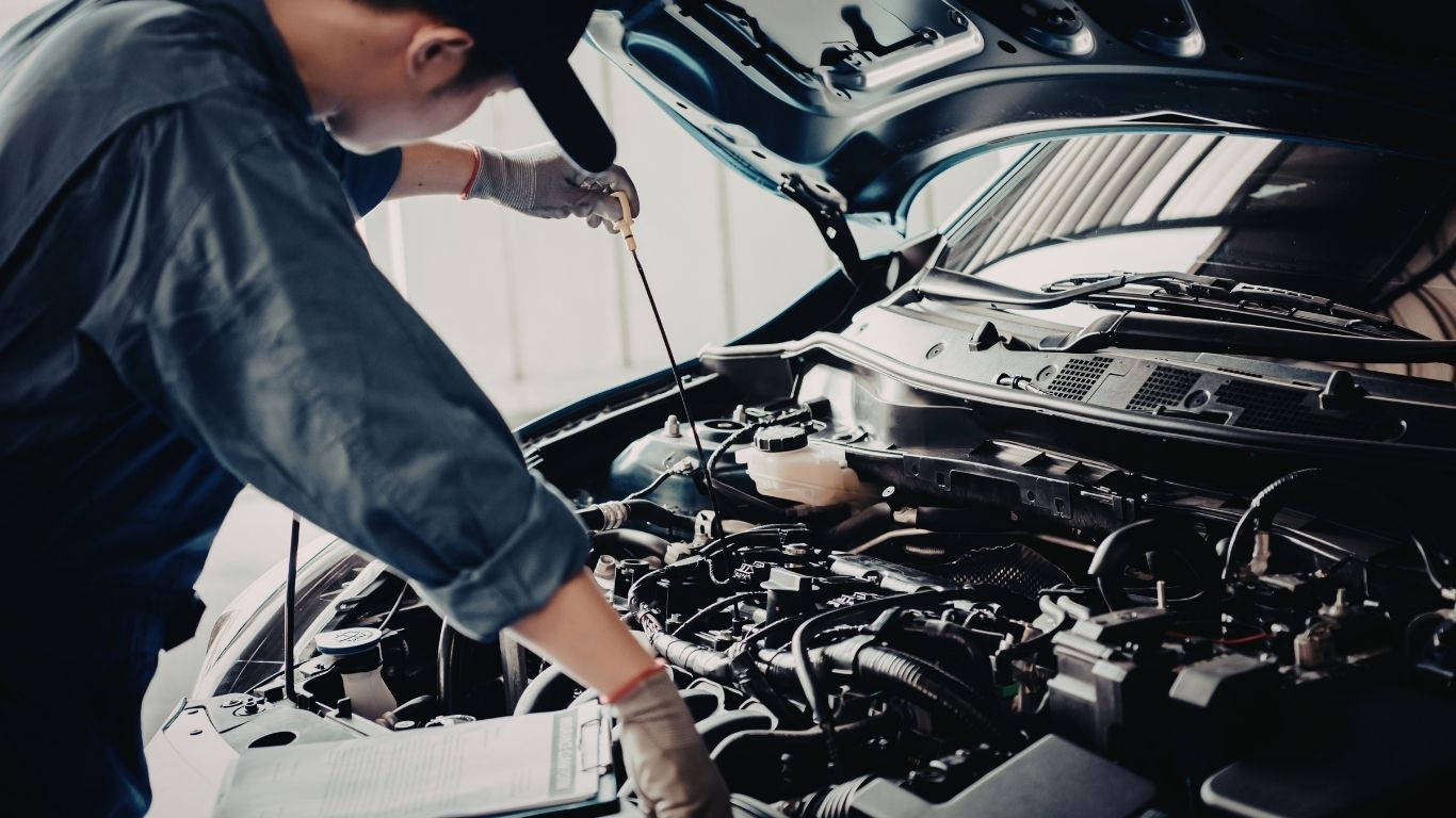 一名身穿藍色制服的機械師正在車庫裡檢查一輛敞開的汽車引擎的機油油位。