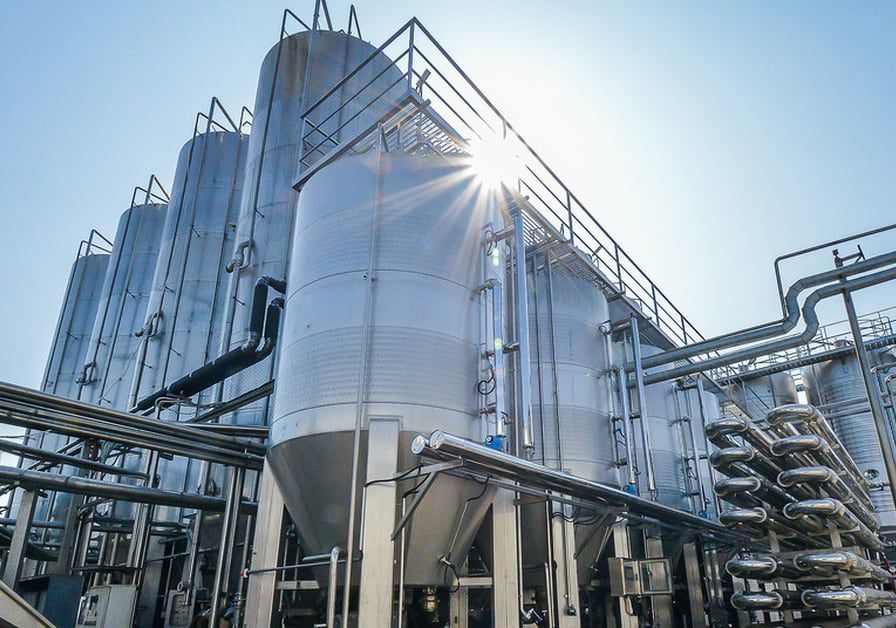 大型工業廠房，銀色的儲存槽、管道，頭頂是明媚的陽光。