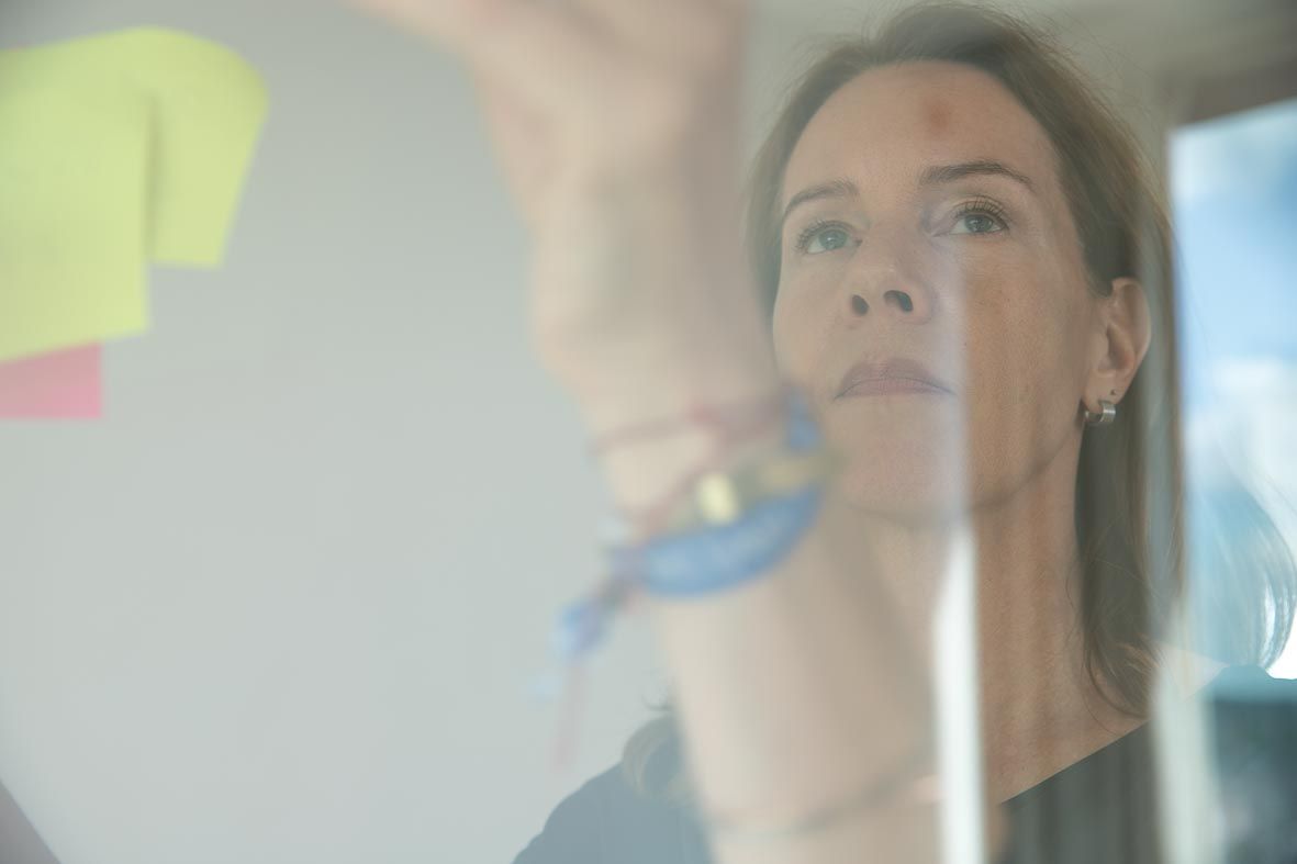 Een vrouw kijkt omhoog terwijl ze met plakbriefjes op een glazen oppervlak schrijft.