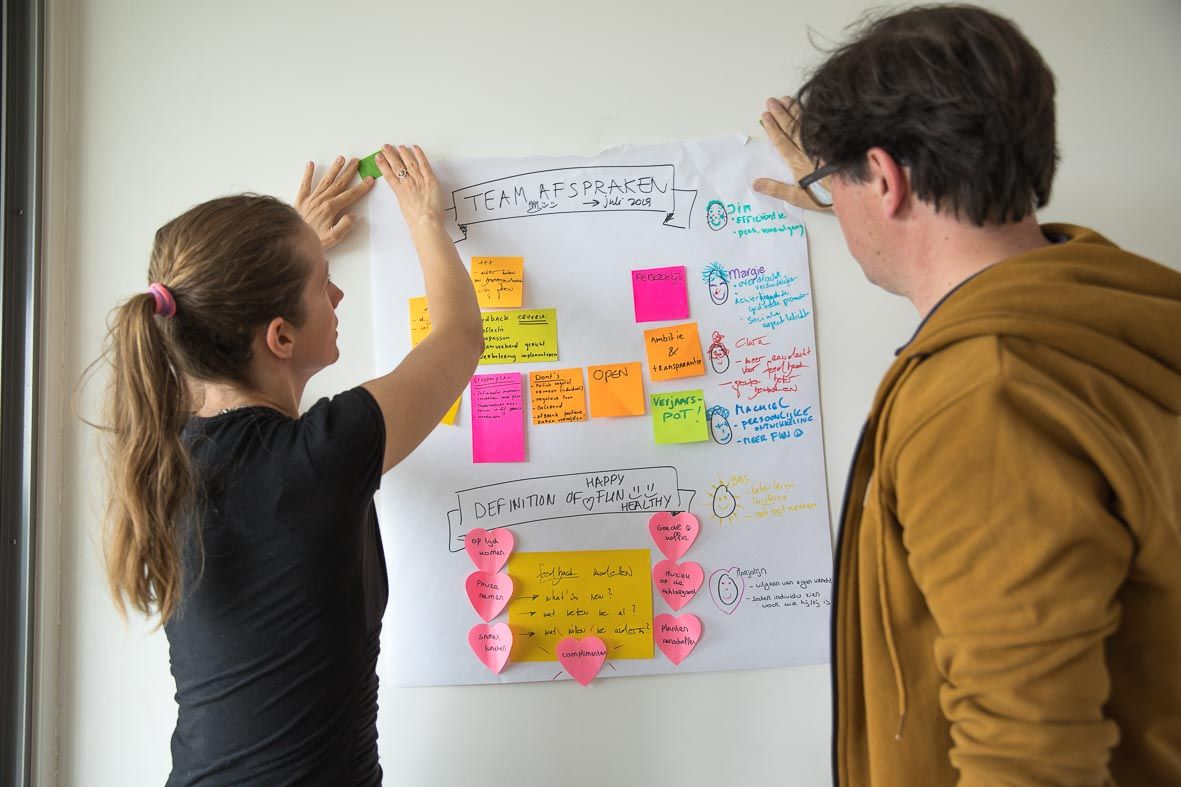 Vier collega's werken samen rond een tafel, bekijken documenten en gebruiken laptops in een kantooromgeving.
