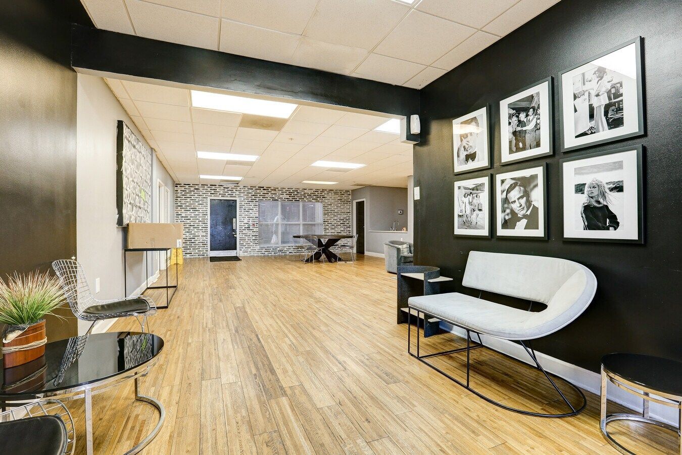 Interior of a studio with bamboo floors, black accent wall, framed photos, white couch, and glass tables.