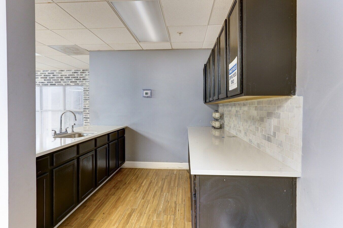 Kitchen with dark cabinets, white countertops, and light wood flooring.