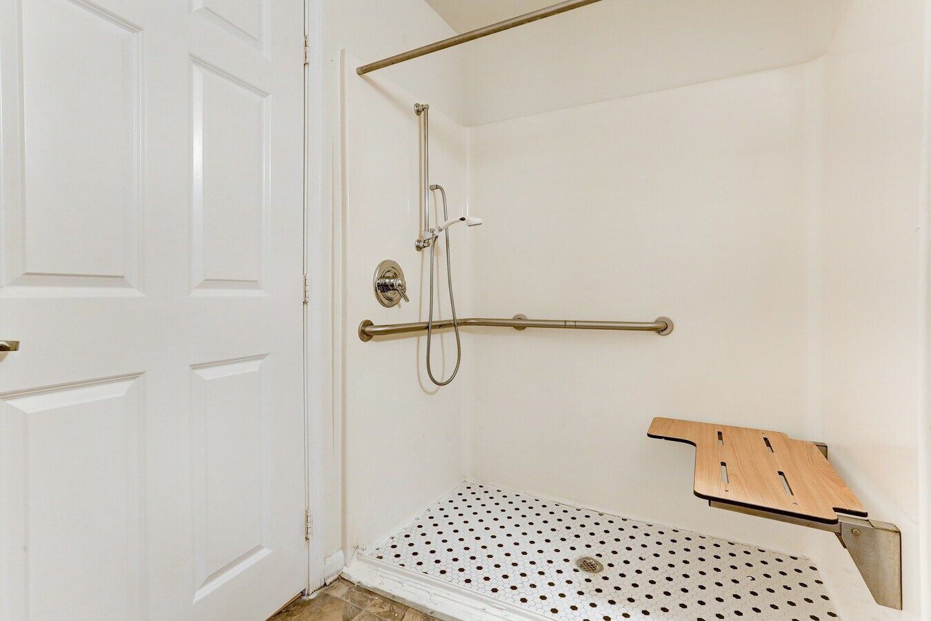 White accessible shower with seat, grab bars, and patterned floor.
