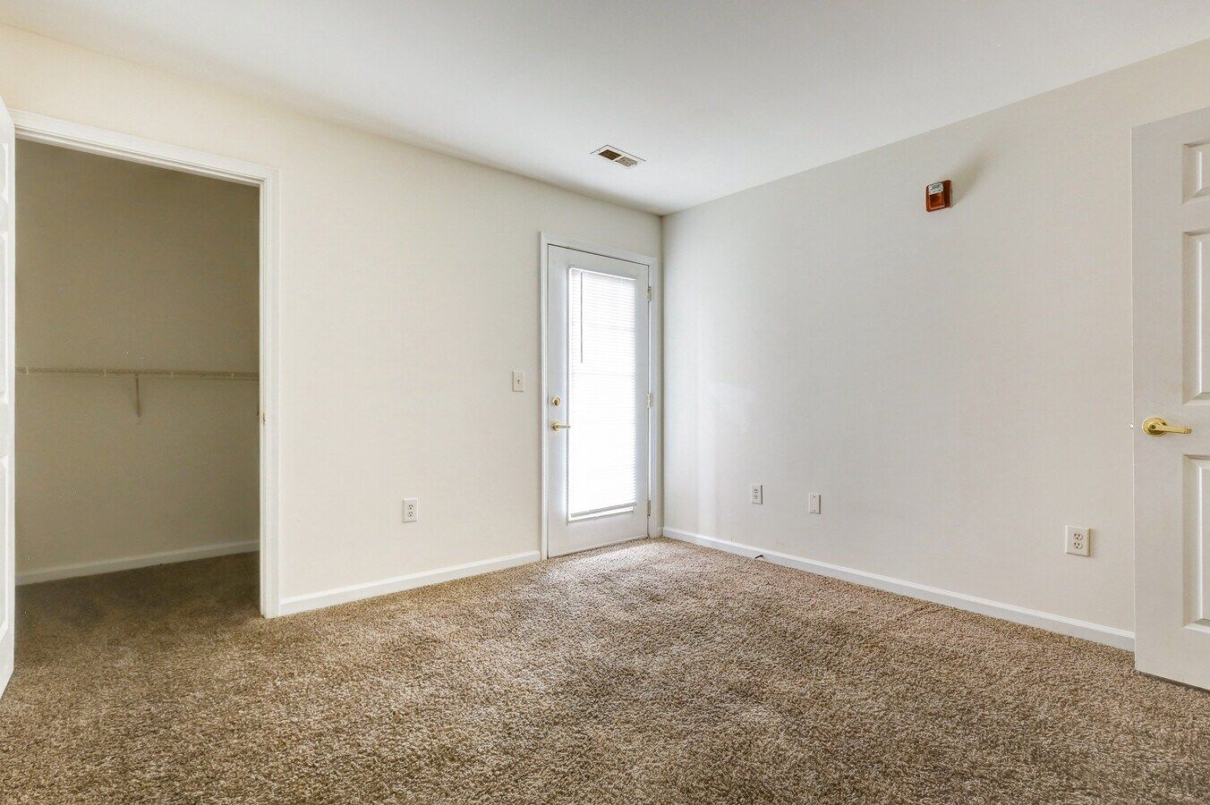 Empty bedroom with brown carpet, white walls, door to outside and closet.