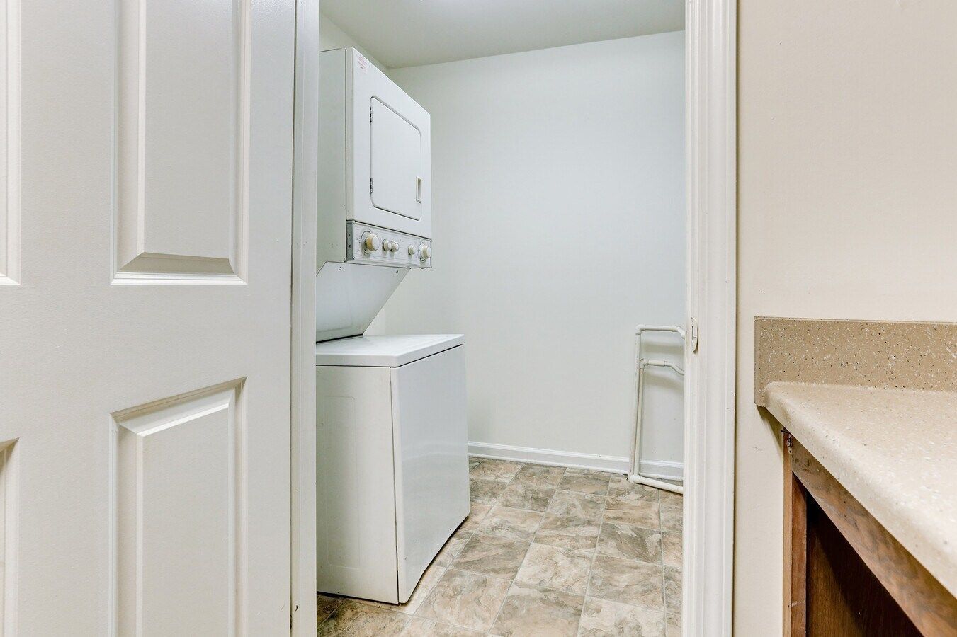 Laundry room with white stacked washer and dryer, neutral flooring, open door.