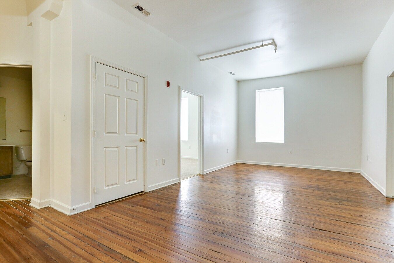Empty room with hardwood floors, white walls, door, and window.