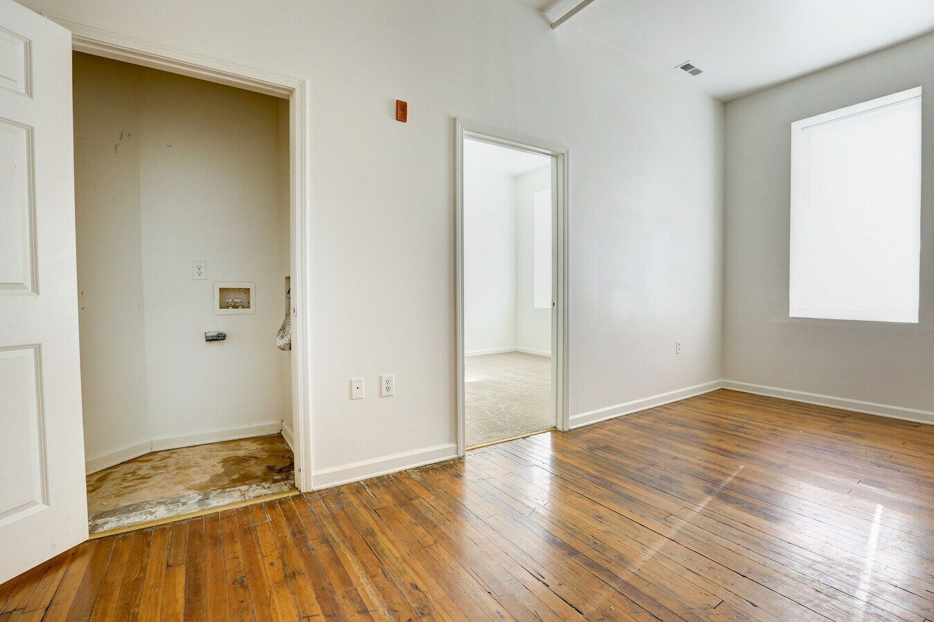 Empty room with wood floor, a laundry closet, and a doorway.