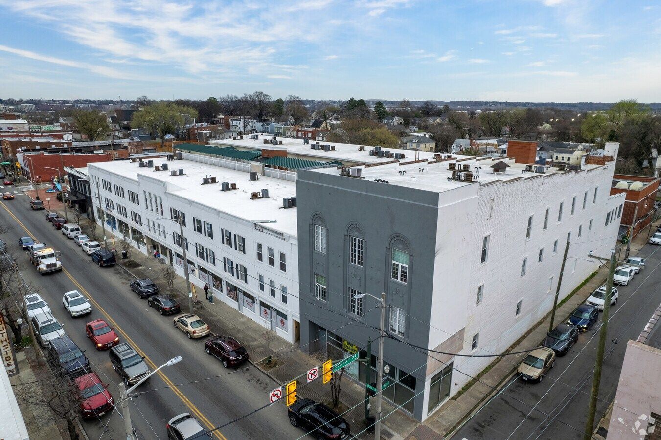 Aerial view of a multi-story building complex, painted white and gray, along a street with parked cars.