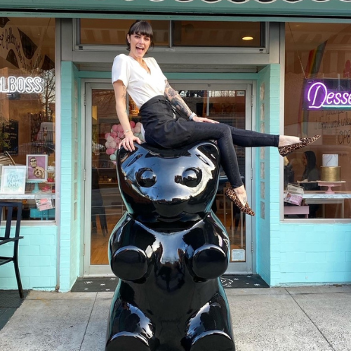 Ashley Holt sitting on top of a large black teddy bear outside of bakery