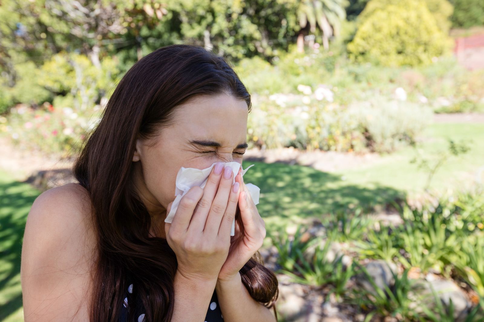 A woman is blowing her nose into a napkin in a park.