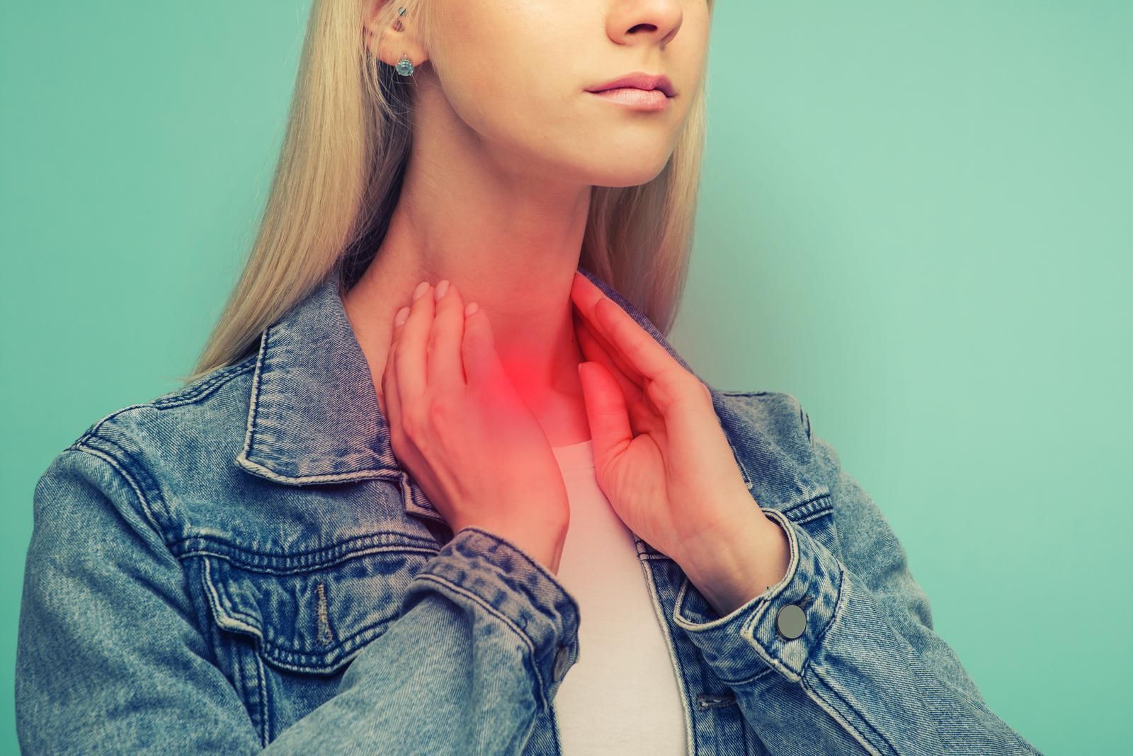 A woman is holding her neck because she has a sore throat and thyroid problems.