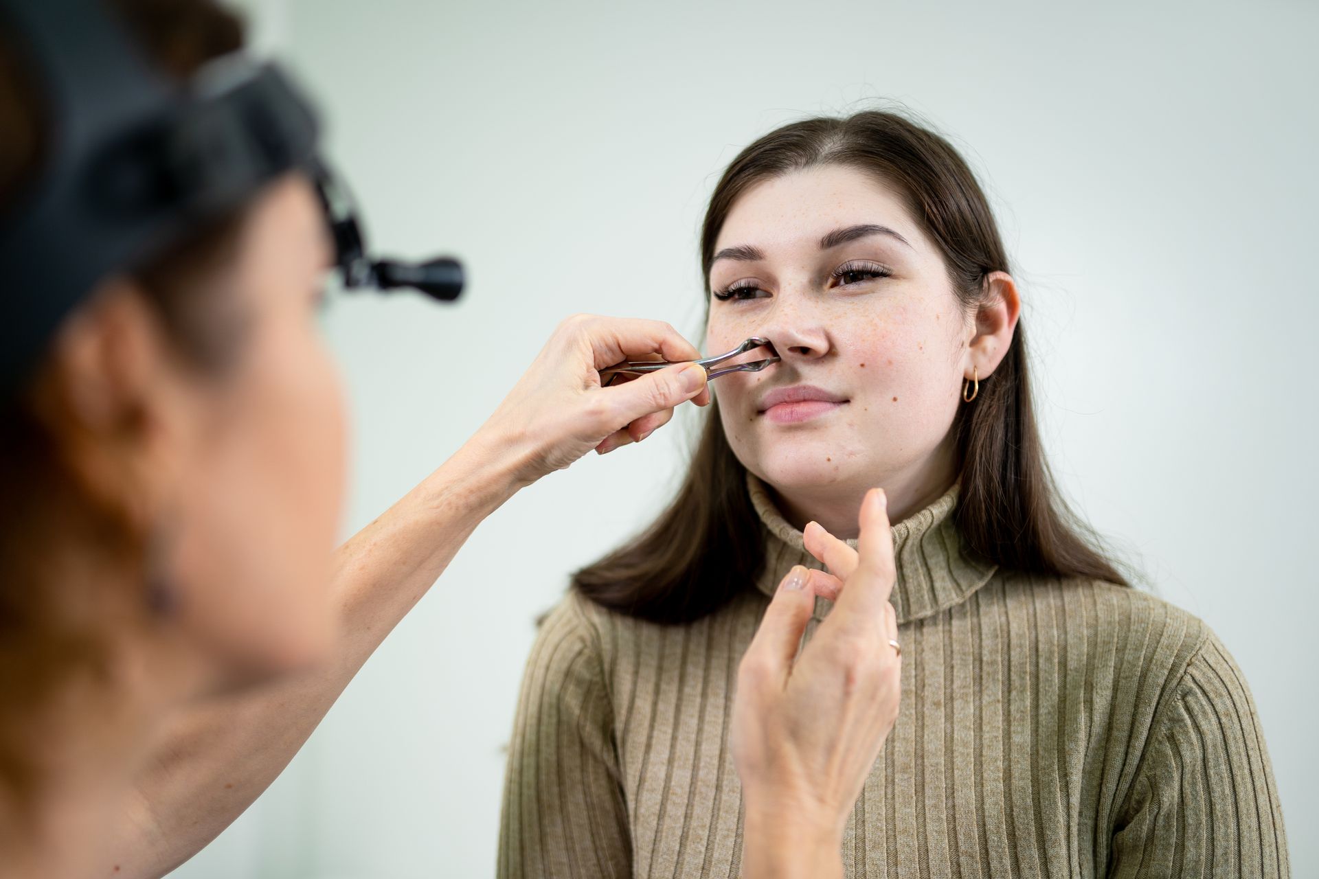 A woman with deviated septum is getting her nose examined by a doctor.