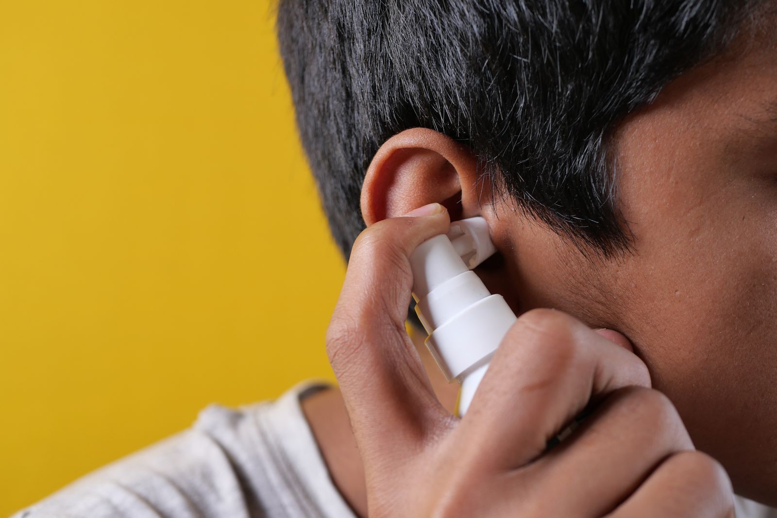 A man is cleaning his ear with a spray bottle.