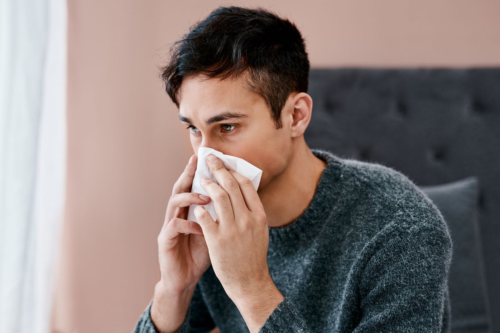 A man is blowing his nose into a napkin while sitting on a couch.