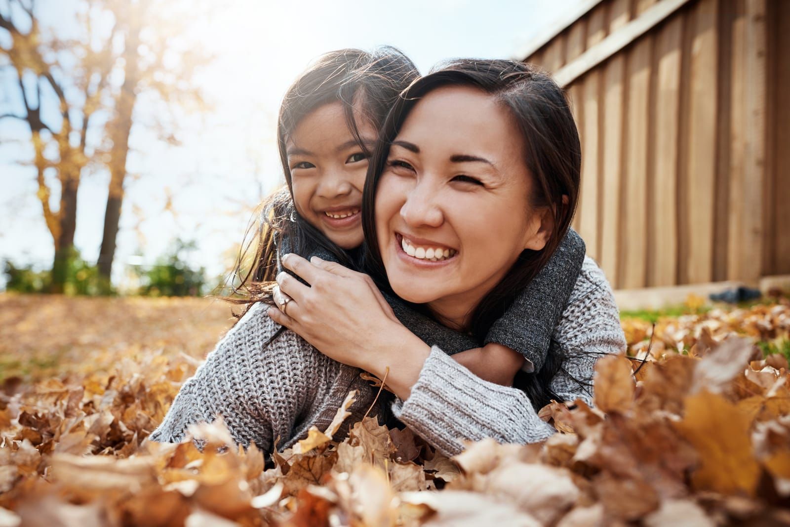 A woman is giving a little girl a piggyback ride while laying in a pile of leaves.