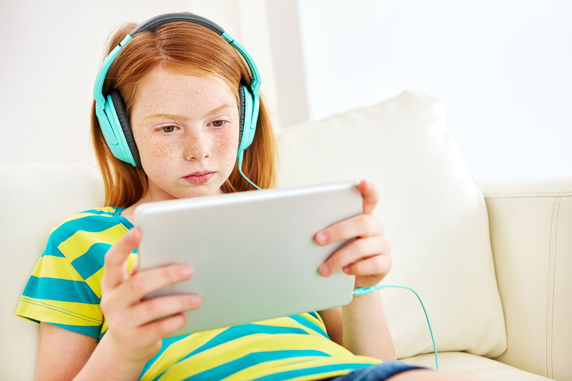 A young girl wearing headphones is using a tablet computer.