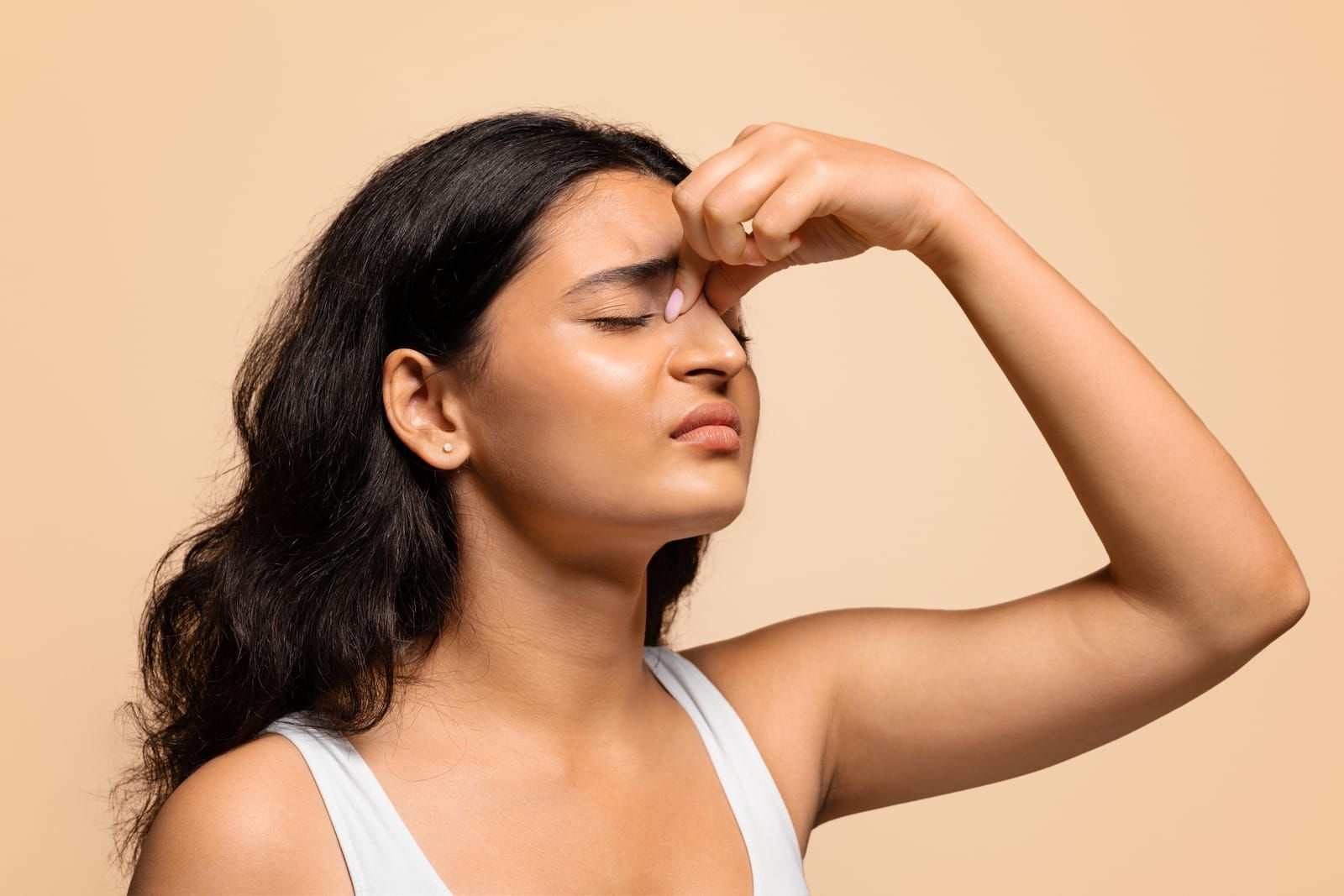 A woman is holding her nose while suffering from nasal congestion and facial pressure.