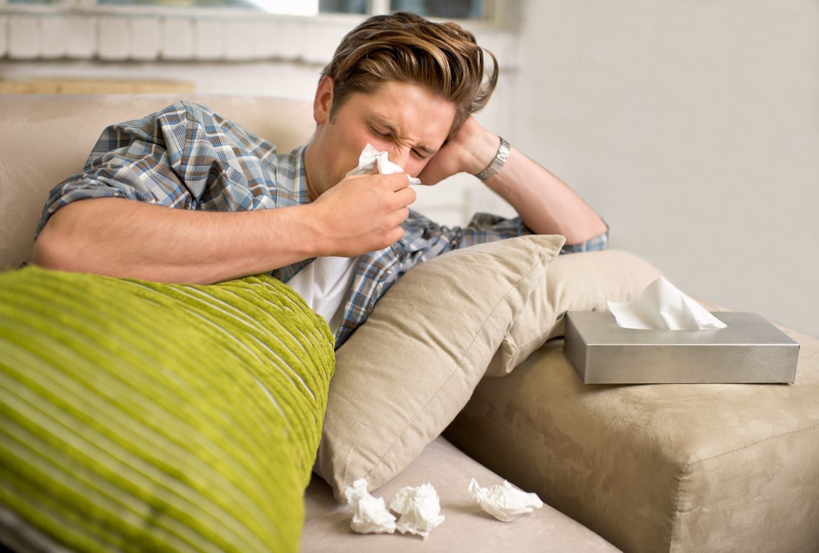 man-sneezing-into-tissue-on-sofa-with-allergies