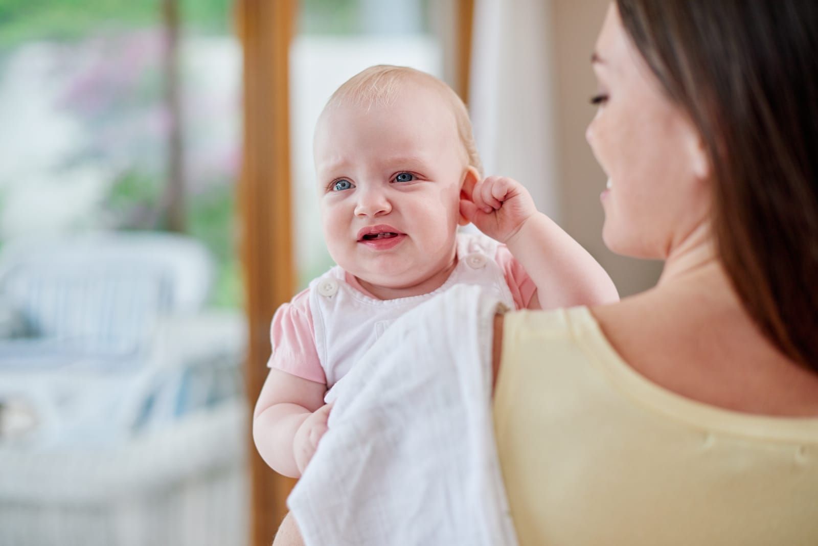 Woman comforting a crying baby with ear infection in her arms.