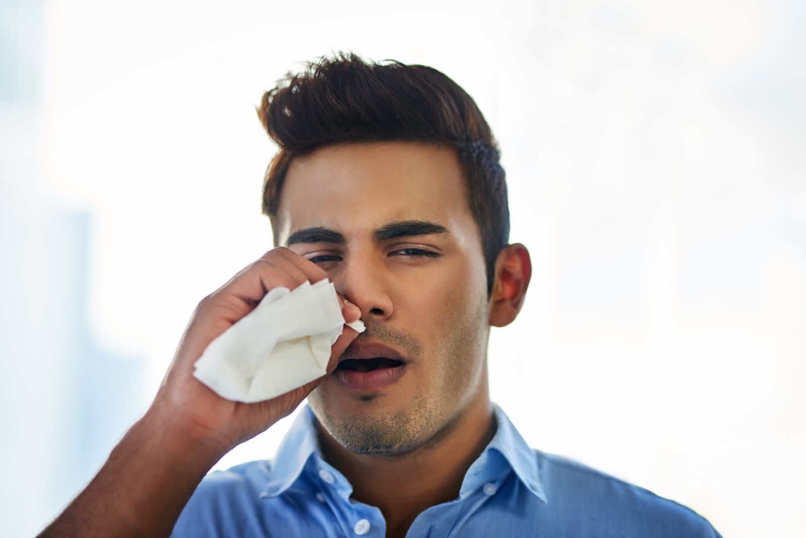 A man suffering from sinus infection is blowing his nose with a napkin.