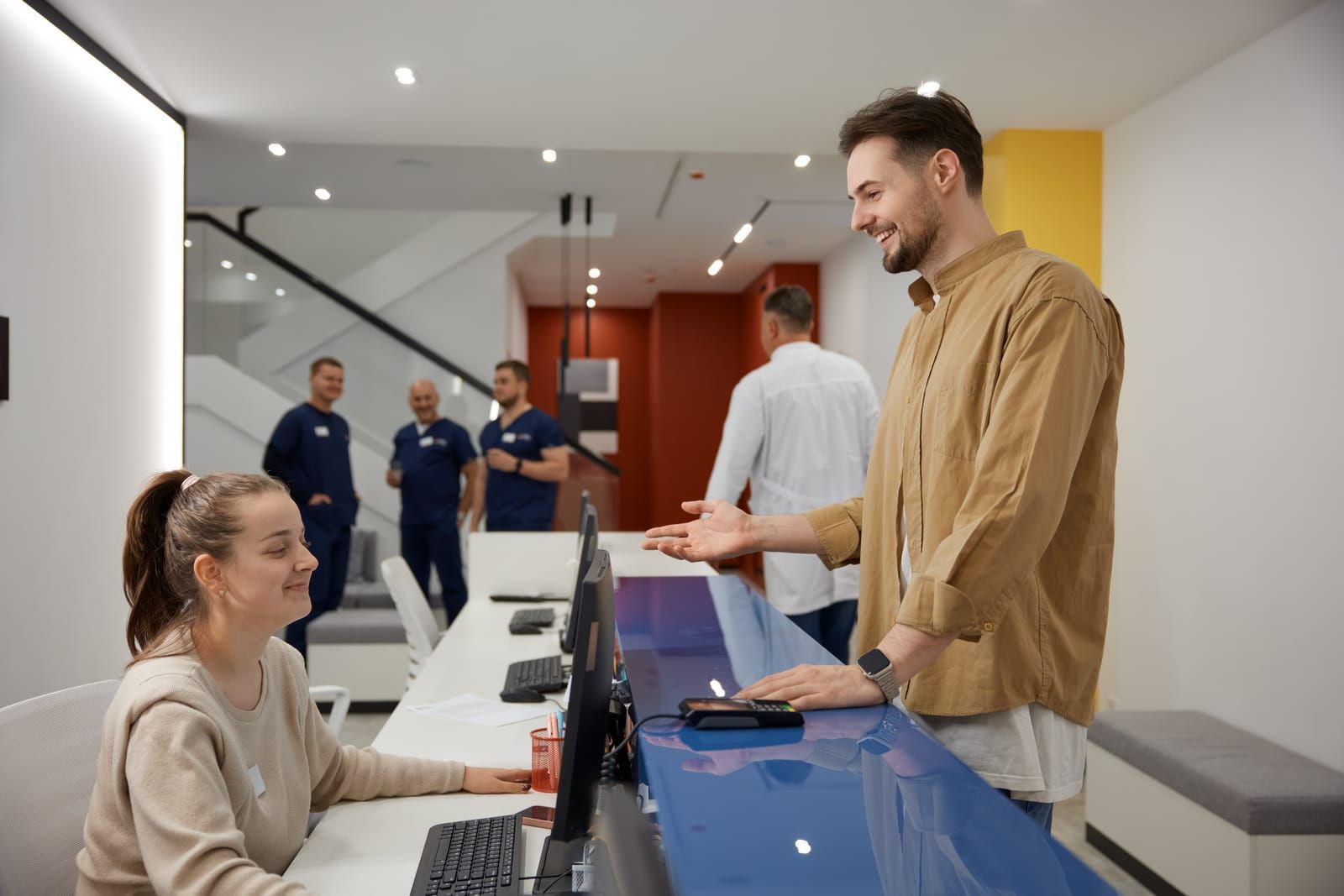 male patient talking-and-smiling-to-nurse-at-reception-in-clinic-waiting-room