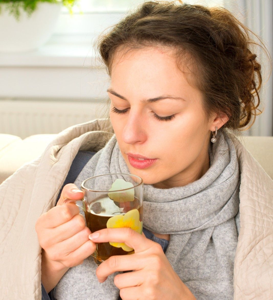 A woman is drinking a cup of tea to help prevent sore throat during cold season.