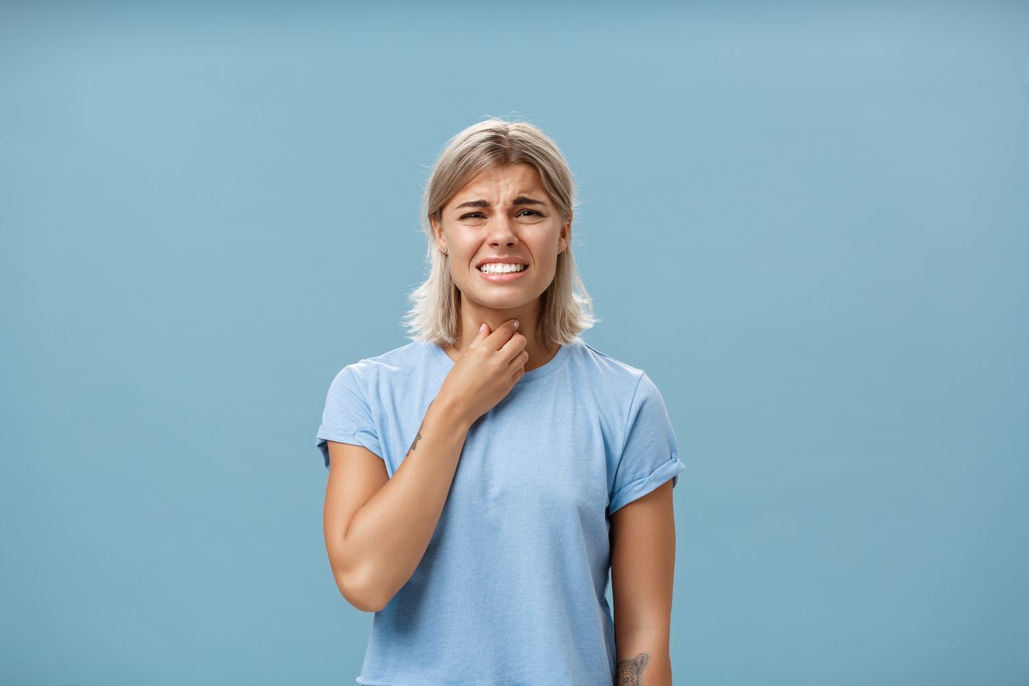 A woman is holding her throat because she has a sore throat.
