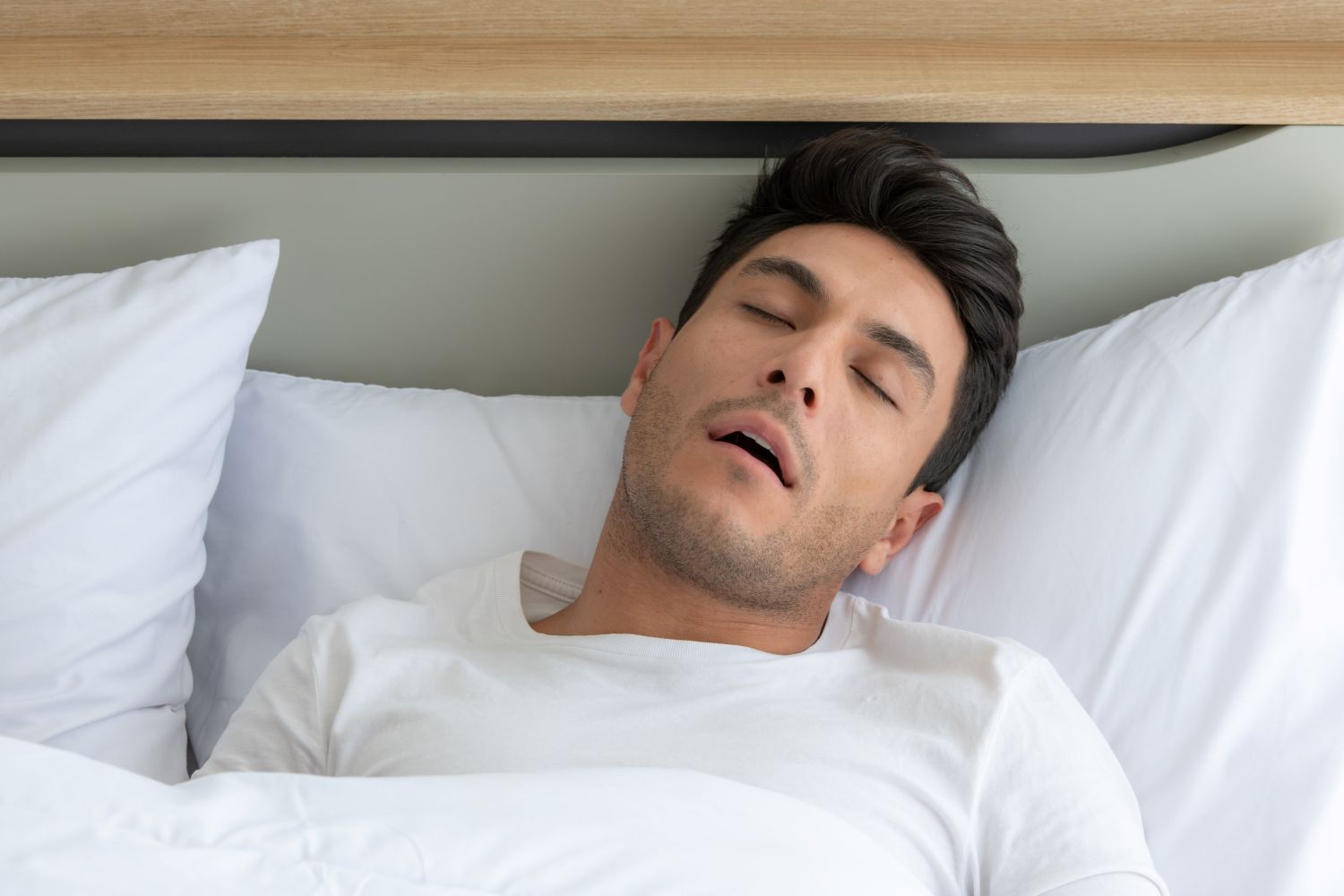 Man sleeping in bed, mouth open. White pillow, sheet, and t-shirt.