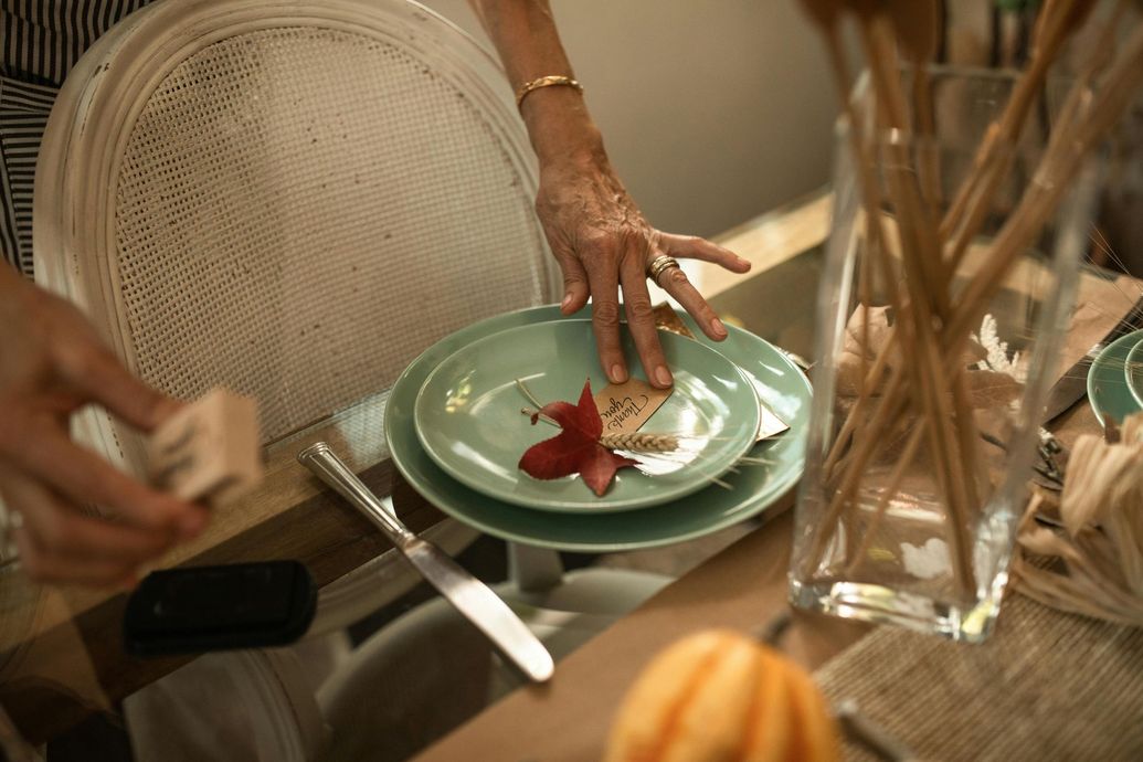 A person is setting a table with plates , utensils , and a vase.